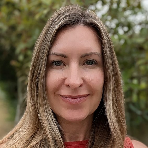 Kellie - ACC Team Member A woman with long, straight hair smiles warmly in a natural outdoor setting.