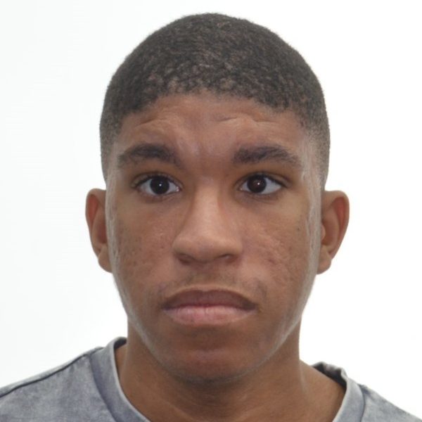 A young man with short hair, wearing a grey top, looking directly at the camera.