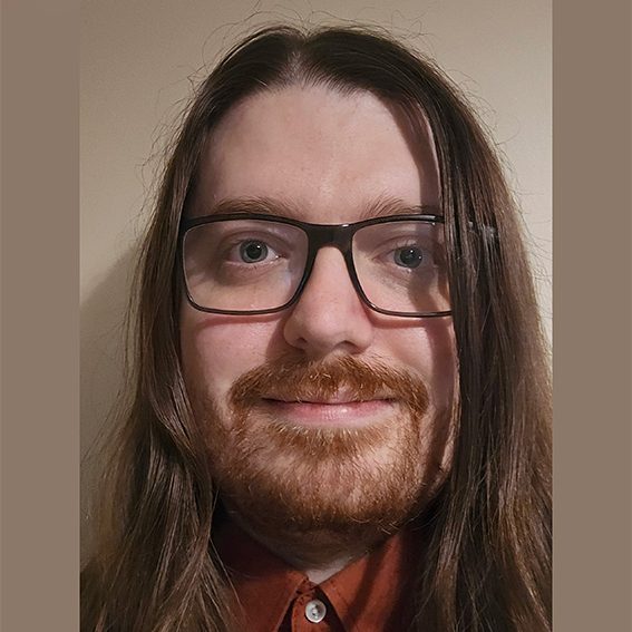 Person with long hair and glasses smiling, wearing a brown shirt.