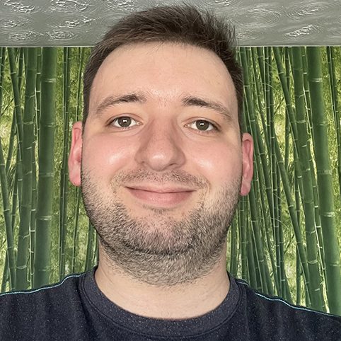 Man with short hair and a beard smiles against a green patterned wall.