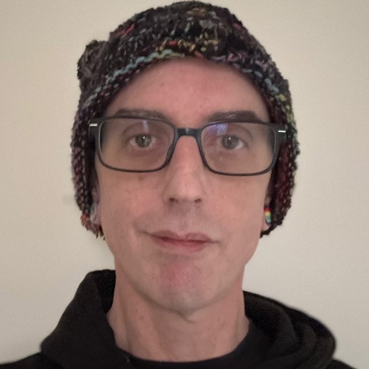 Person wearing glasses and a patterned beanie, facing forward with a neutral expression.