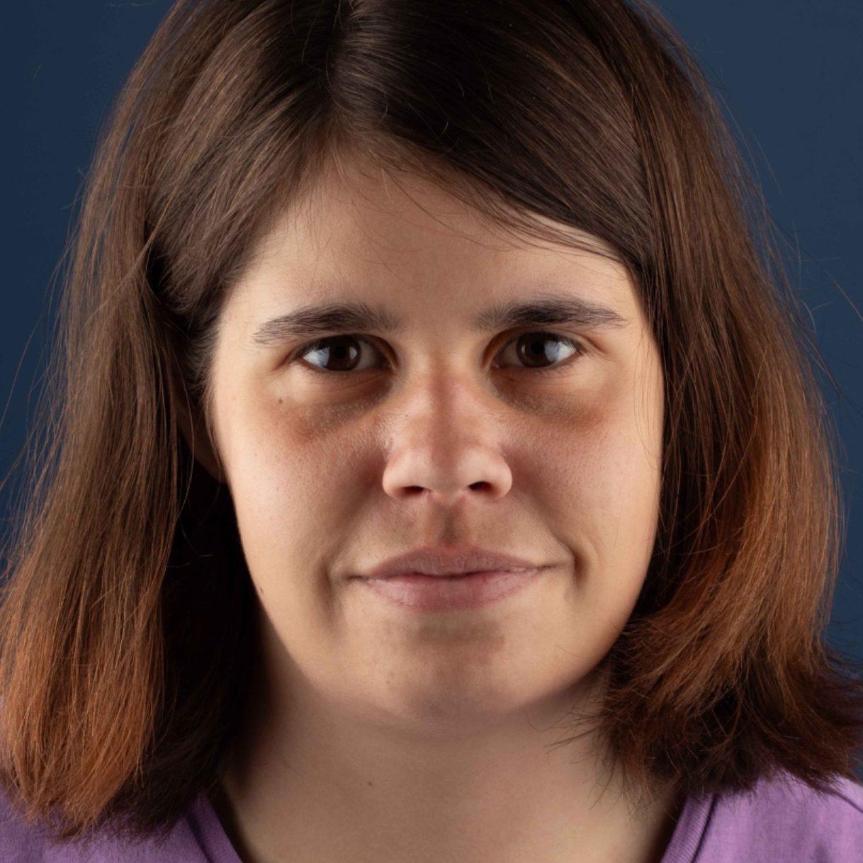 Woman with shoulder-length brown hair, wearing a purple top, and looking directly at the camera.
