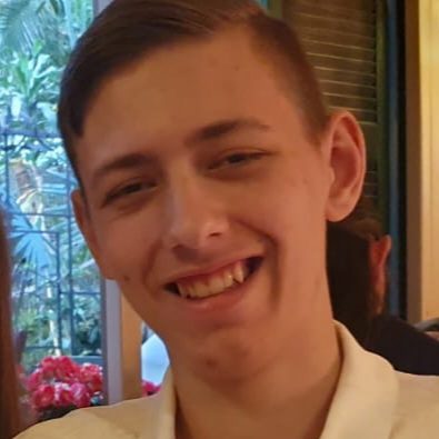 Smiling young man in a light shirt, with greenery in the background.