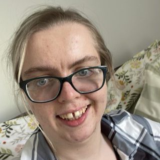Smiling person with glasses, light brown hair, wearing a checked shirt.