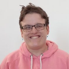 Smiling person in a pink hoodie with glasses and short hair.