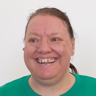 A woman with long brown hair and a bright green top smiling warmly.