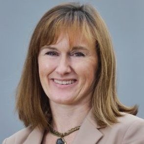 Smiling woman with shoulder-length brown hair, wearing a blazer and a necklace.