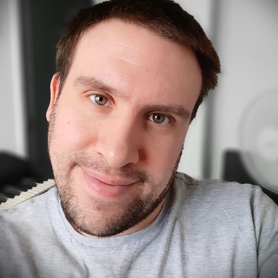 Man with short brown hair and light stubble, smiling at the camera.