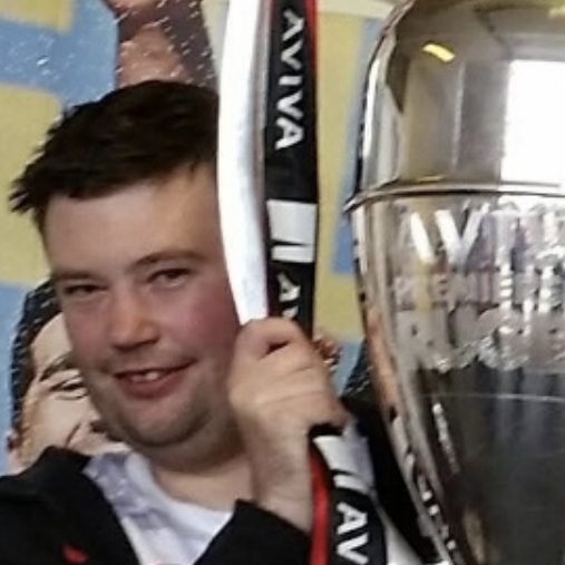Person holding a trophy with a smiling expression, wearing a dark jacket.