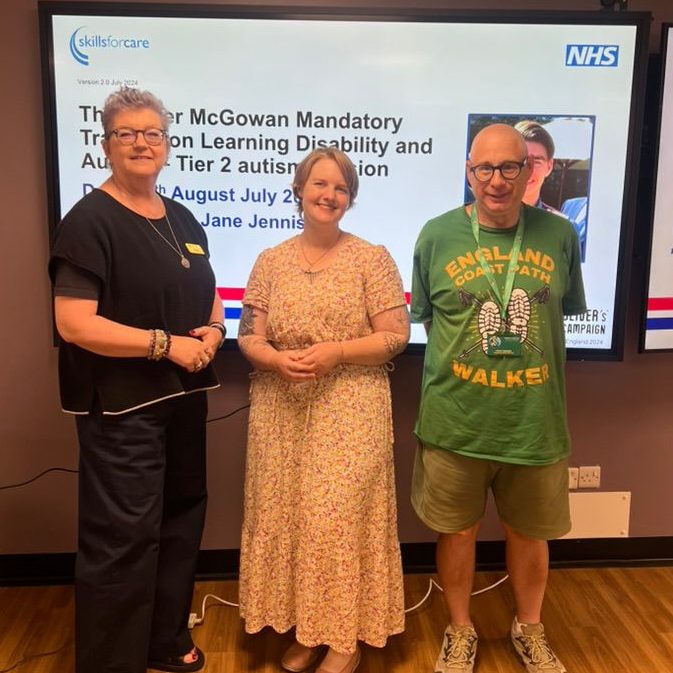 3 people stood in front of large monitor.