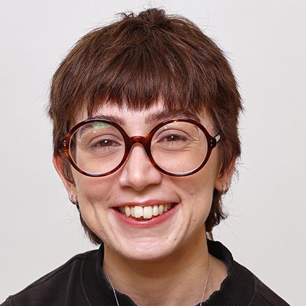 Nellie - ACC Co-Trainer Young person with short brown hair and round glasses, smiling against a plain background.